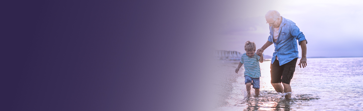 Starejši moški in deček čofotata v morski plitvini.