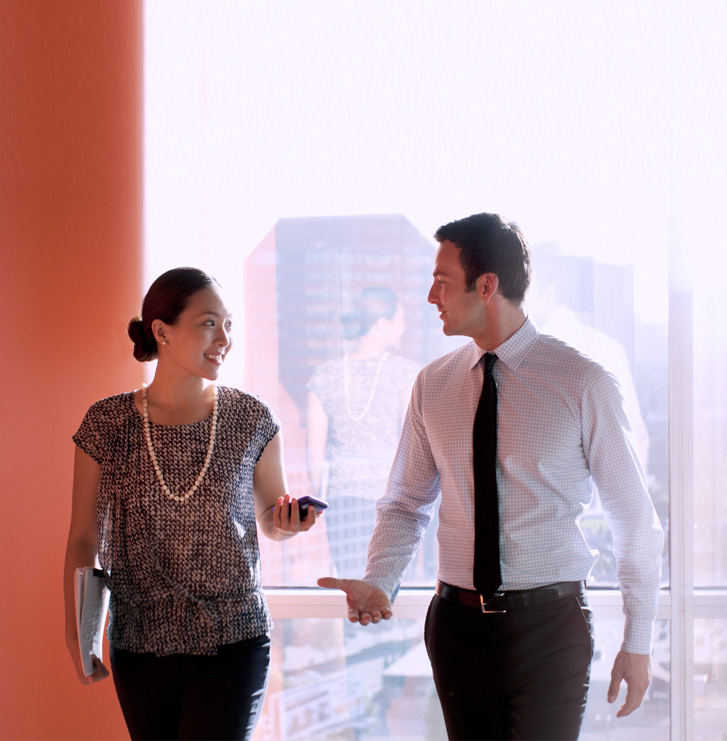 Sodelavca v poslovnih oblačilih med hojo razpravljata o idejah.