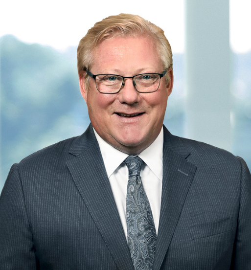 Portret Scotta A. Smitha, izvršnega direktorja, srednjih let, z očali, oblečenega v sivo obleko, ki stoji pred zamegljenim ozadjem pisarne.